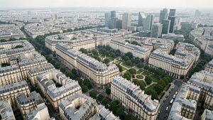Vue aérienne réaliste de Paris montrant le contraste entre les immeubles haussmanniens et les quartiers urbains du nord-est, sous une lumière douce.